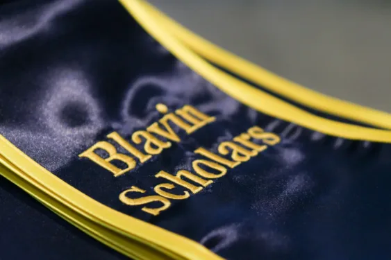 Close-up of folded blue graduation stoles with maize trim, featuring embroidered maize text that reads “Blavin Scholars.”