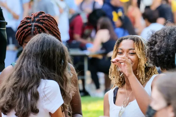 Three students are talking and laughing at a crowded outside event